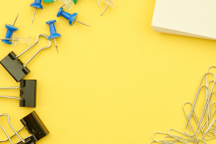 Push pins, binder clips and paper clips scattered on a yellow surface