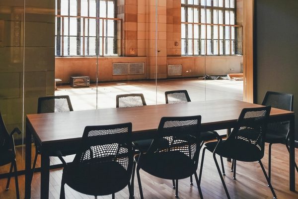 An empty conference table with black chairs beside tall arched windows