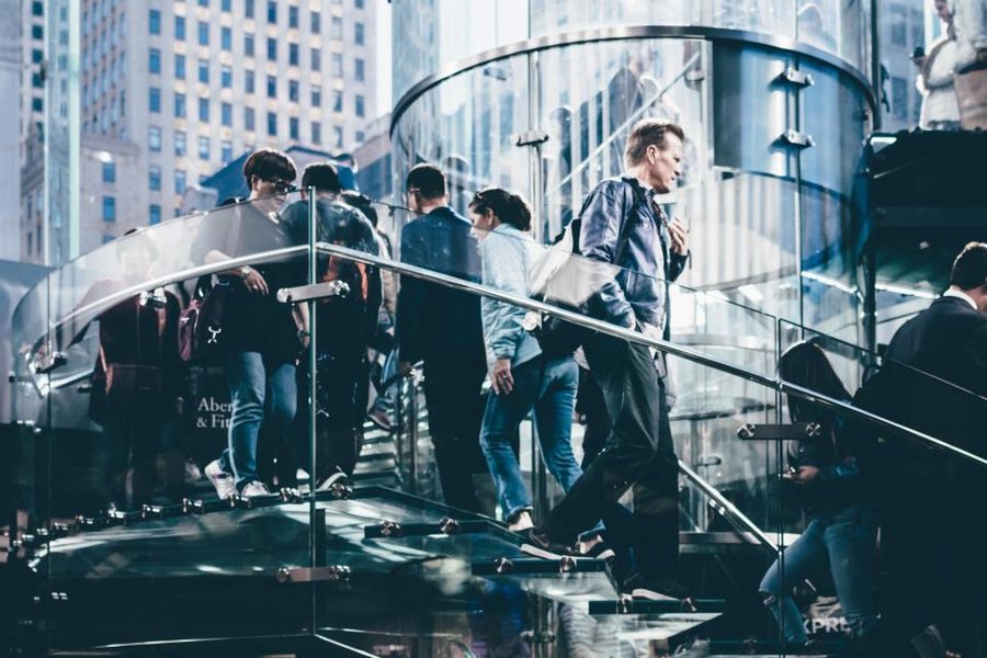 A crowd of people descending an outdoor staircase between glass-fronted city buildings