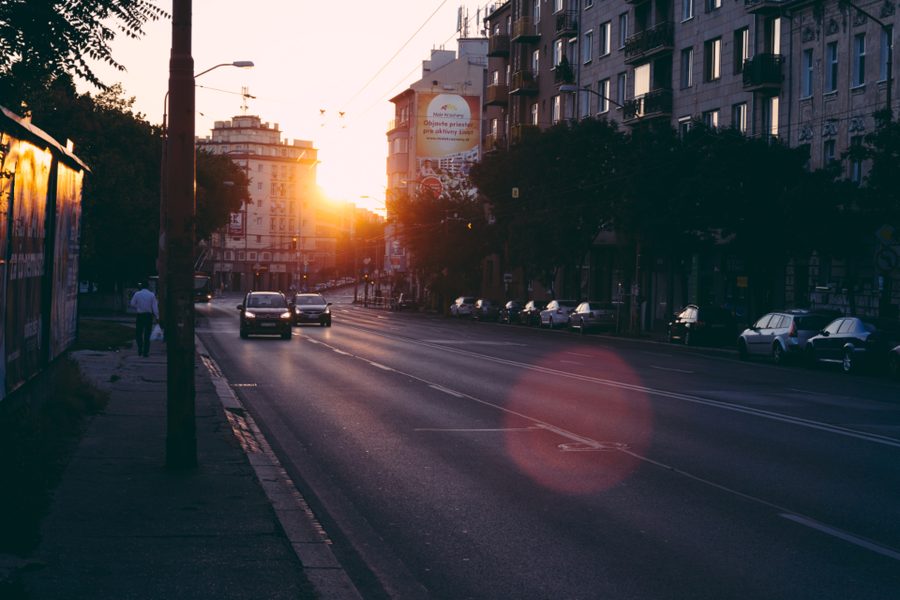 A city street at sunrise with cars, a lamp post and buildings lit by low sunlight