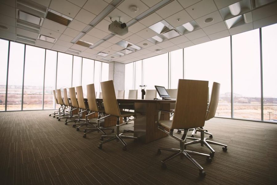 An empty conference room with a long wooden table, wheeled chairs and a city view through tall windows