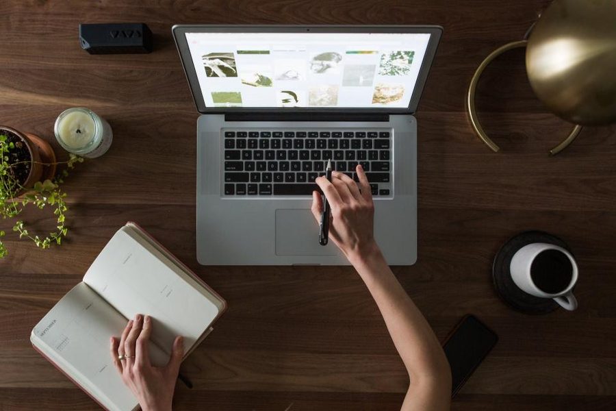 An overhead view of a laptop, an open notebook, a coffee cup and a small plant on a desk