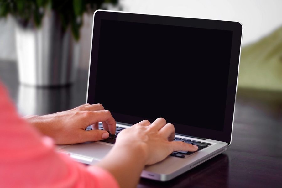 A pair of hands typing on a laptop keyboard with a blank dark screen