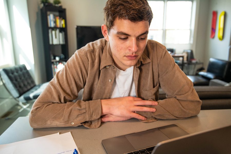A young man resting his chin on his hand looking at a laptop at a home desk
