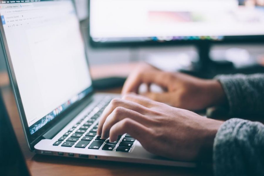 A close view of hands typing on a laptop keyboard with a second monitor in the background