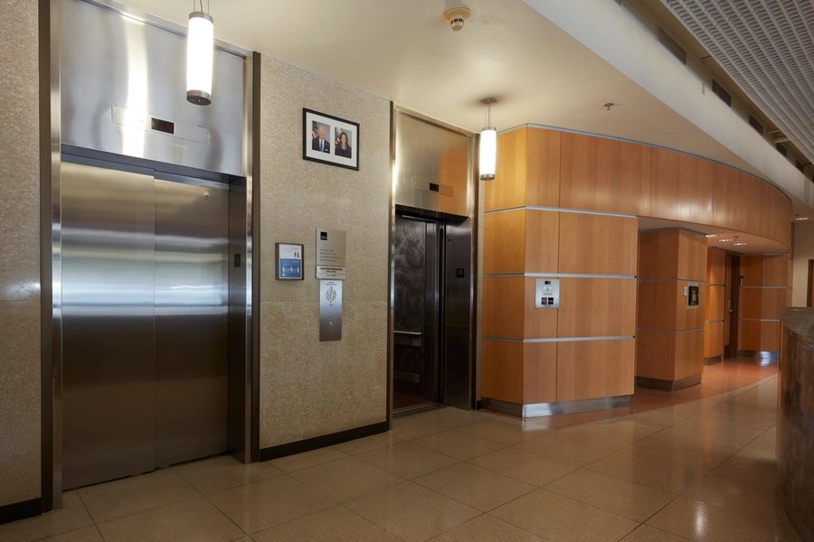 A building lobby with steel elevator doors, wood panelling and framed pictures on the wall