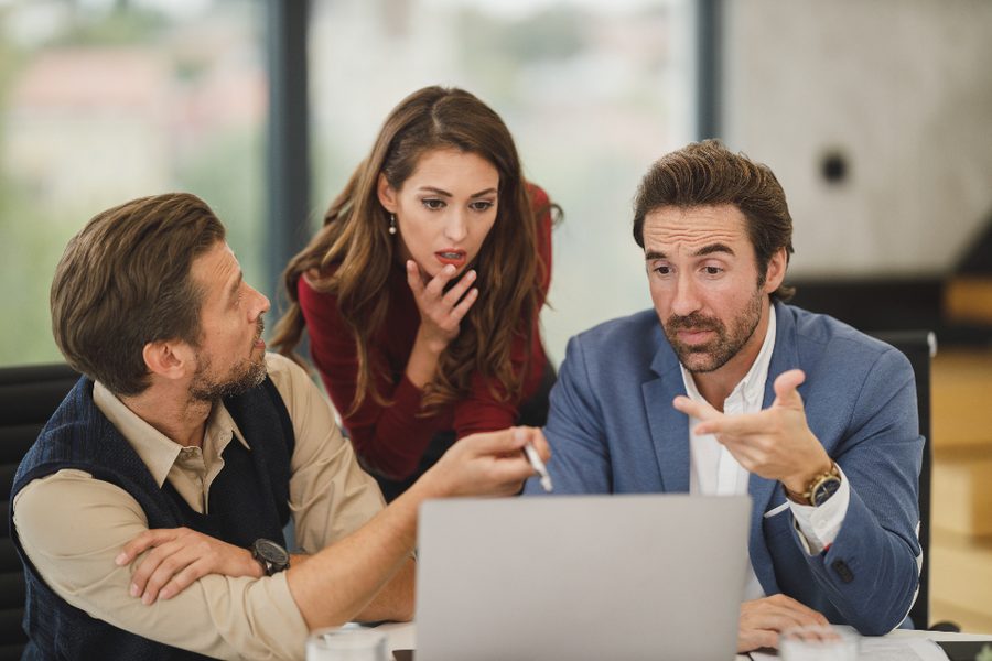 Three colleagues looking at a laptop together, one gesturing while speaking